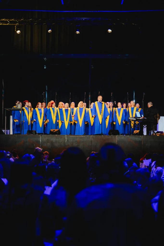 Gospelchor in blau-gelben Roben singt auf einer Bühne vor Publikum bei einer Firmenveranstaltung.