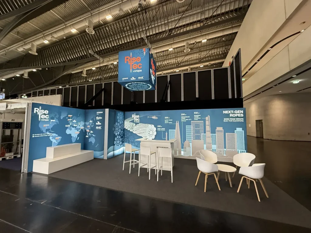 RiseTec-Messestand mit hängendem Leuchtwürfel, Weltkarten-Wand und Sitzbereich, gebaut von Concept Marketing auf der Interlift Nürnberg.