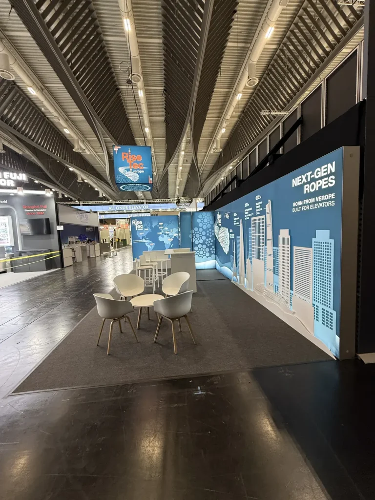 Seitenansicht des RiseTec-Messestands mit Skyline-Illustration und Loungebereich in der Messehalle.