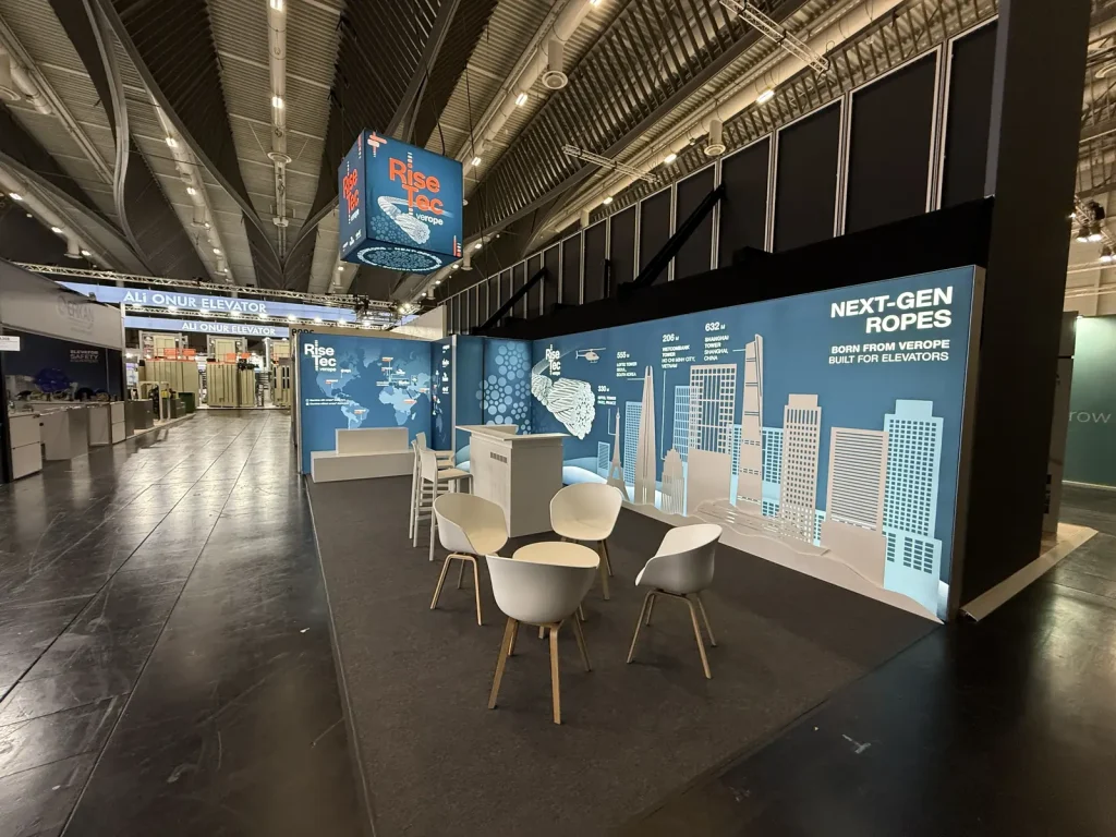 RiseTec-Messestand mit Leuchtwürfel-Signage und Sitzgruppe in der Interlift-Messehalle.