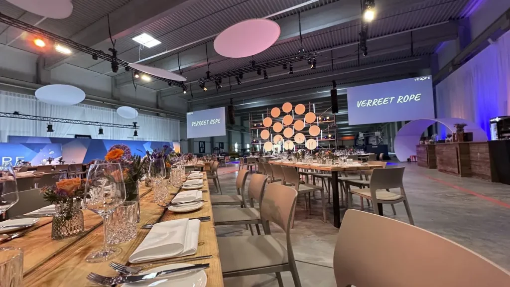 Festlich gedeckte Tafel in einer Industriehalle mit Bühnenaufbau und Videoleinwänden für die VEROPE-Jubiläumsfeier.