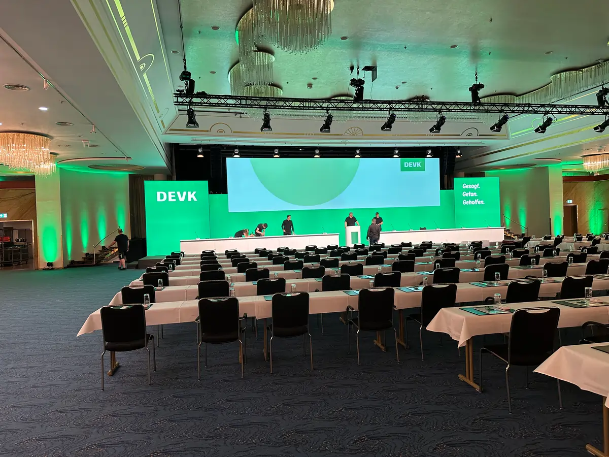 Bestuhlter Veranstaltungssaal der DEVK Location mit beleuchtetem Podium und Markenelementen, professionell umgesetzt durch deine Eventagentur St. Ingbert.
