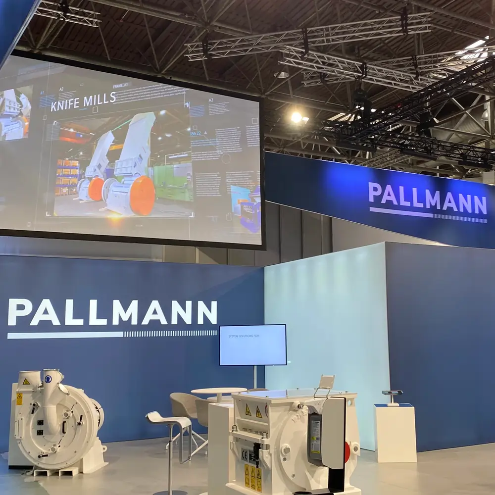 Pallmann-Messestand mit Maschinenexponaten und Präsentationsleinwand in einer Ausstellungshalle.