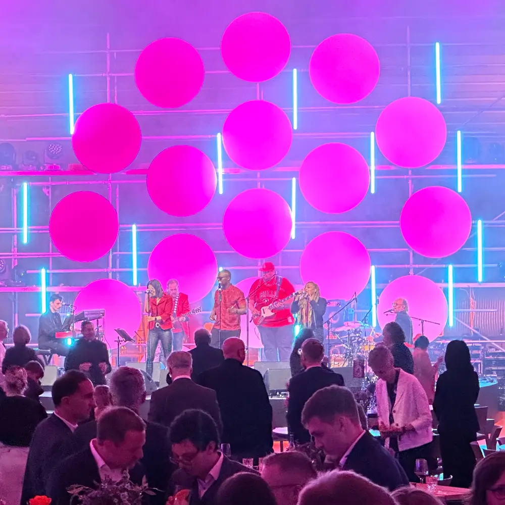 Liveband tritt vor pinker Kreis-Lichtinstallation auf, Gäste feiern bei einer Firmenveranstaltung.