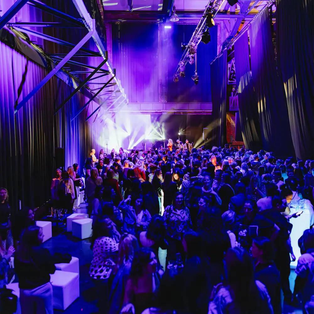 Publikum bei einer nächtlichen Firmenfeier in violettem Bühnenlicht mit Liveband im Hintergrund.